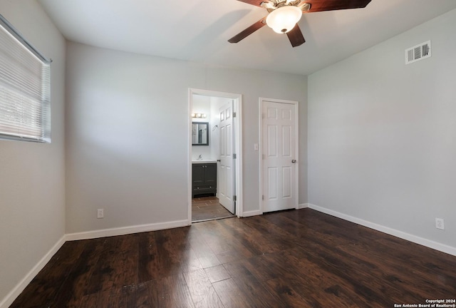 unfurnished bedroom with ensuite bathroom, a closet, ceiling fan, and dark wood-type flooring