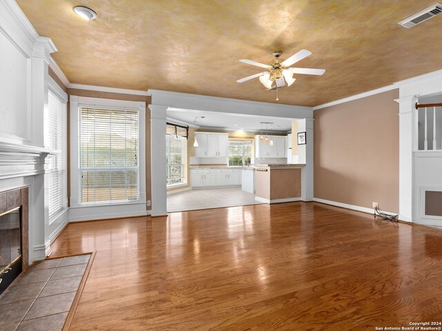 unfurnished living room with light wood-type flooring, ornamental molding, and a tiled fireplace