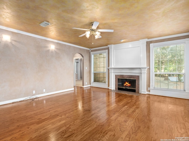 unfurnished living room featuring hardwood / wood-style floors, ceiling fan, ornamental molding, and a tiled fireplace