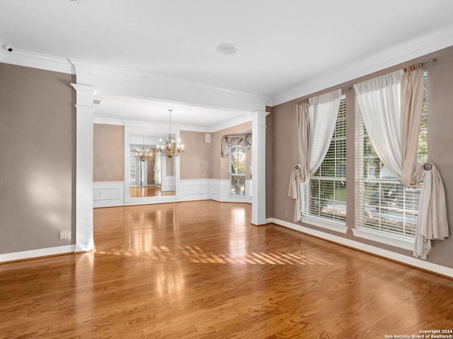 unfurnished living room featuring decorative columns, crown molding, hardwood / wood-style floors, and an inviting chandelier