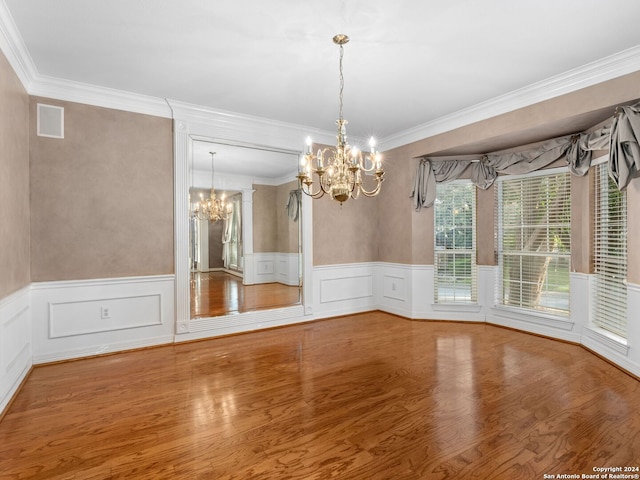 unfurnished dining area featuring hardwood / wood-style floors, crown molding, and a chandelier