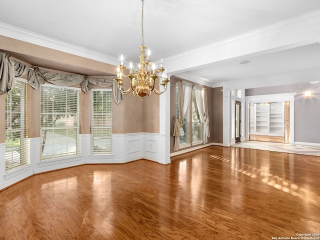 unfurnished dining area with decorative columns, ornamental molding, a chandelier, and hardwood / wood-style flooring