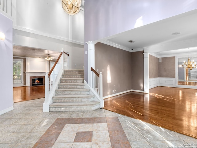 staircase featuring a high ceiling, decorative columns, wood-type flooring, ceiling fan with notable chandelier, and ornamental molding