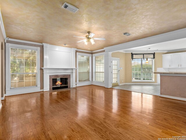 unfurnished living room with light hardwood / wood-style flooring, ceiling fan, crown molding, and a tiled fireplace