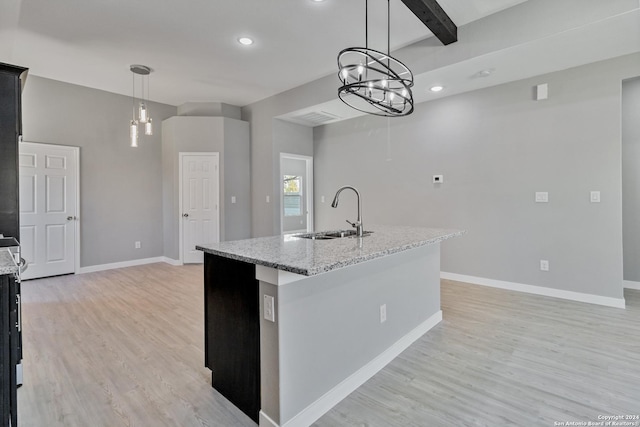 kitchen with a center island with sink, sink, light hardwood / wood-style flooring, light stone countertops, and decorative light fixtures