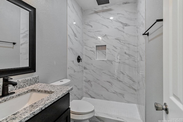 bathroom with a tile shower, vanity, and toilet