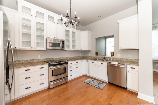 kitchen featuring appliances with stainless steel finishes, light wood-type flooring, sink, pendant lighting, and white cabinetry