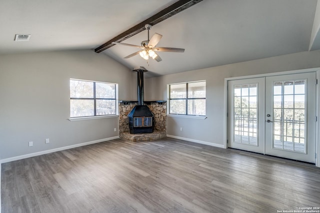 unfurnished living room featuring light wood-type flooring, lofted ceiling with beams, a wood stove, and a wealth of natural light