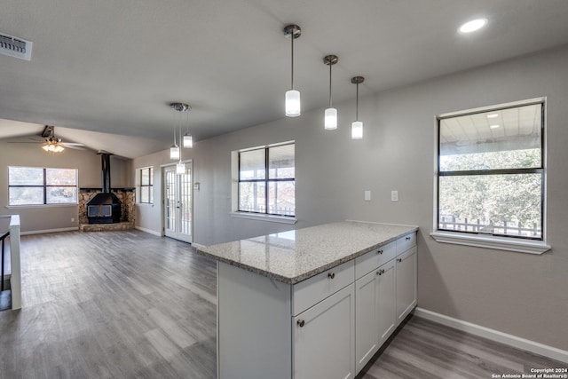 kitchen with light stone countertops, white cabinets, hardwood / wood-style floors, a wood stove, and hanging light fixtures