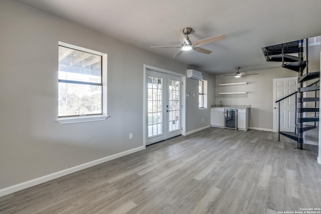 unfurnished living room featuring a wall mounted air conditioner, french doors, ceiling fan, light hardwood / wood-style floors, and wine cooler