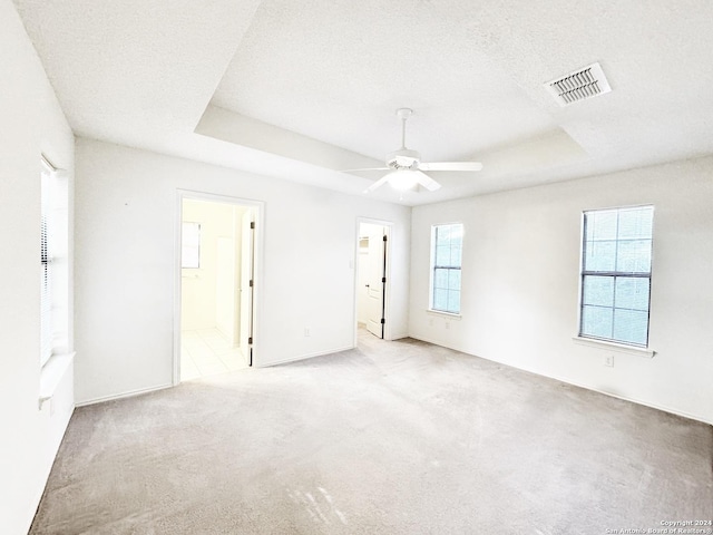 spare room featuring a raised ceiling, ceiling fan, light colored carpet, and a textured ceiling