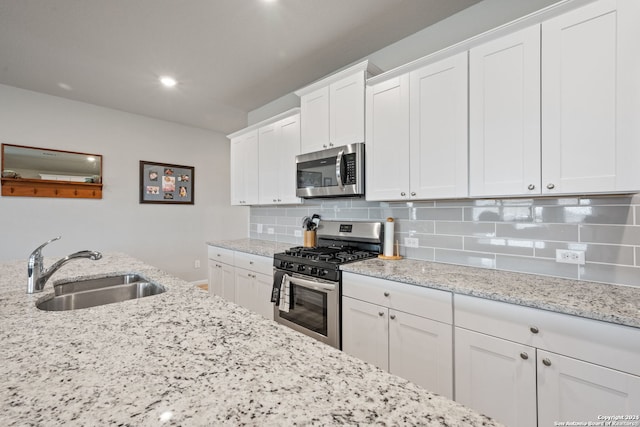 kitchen featuring light stone countertops, tasteful backsplash, stainless steel appliances, sink, and white cabinets