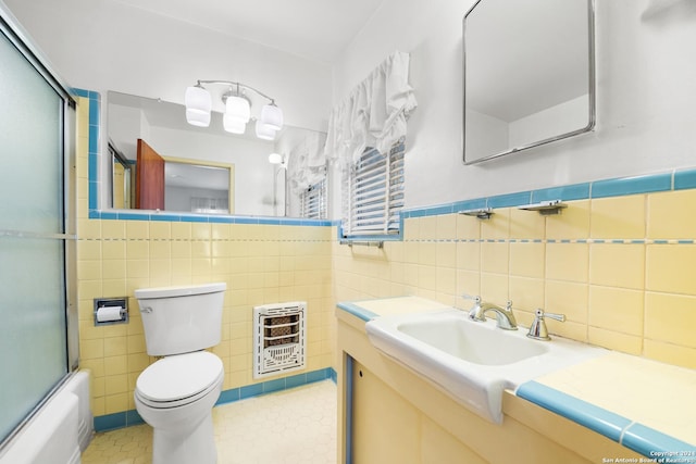 full bathroom with vanity, shower / bath combination with glass door, toilet, tile walls, and heating unit