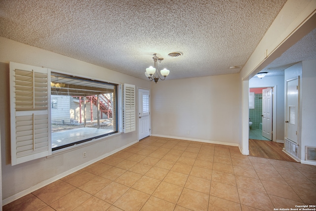 unfurnished room with light tile patterned flooring, a textured ceiling, and a chandelier