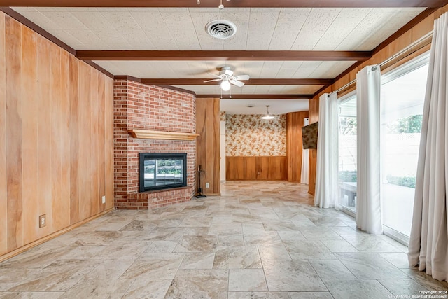 unfurnished living room with beamed ceiling, ceiling fan, wood walls, and a brick fireplace