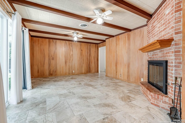 unfurnished living room with beam ceiling, ceiling fan, wood walls, and a brick fireplace