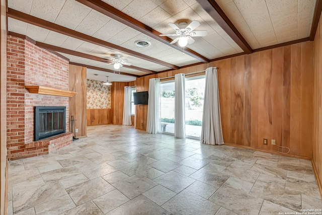 unfurnished living room with beam ceiling, wood walls, a fireplace, and ceiling fan