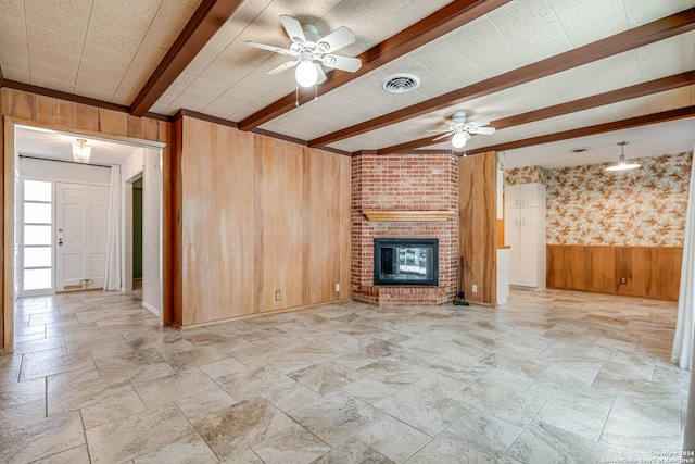 unfurnished living room with beam ceiling, wooden walls, a fireplace, and ceiling fan