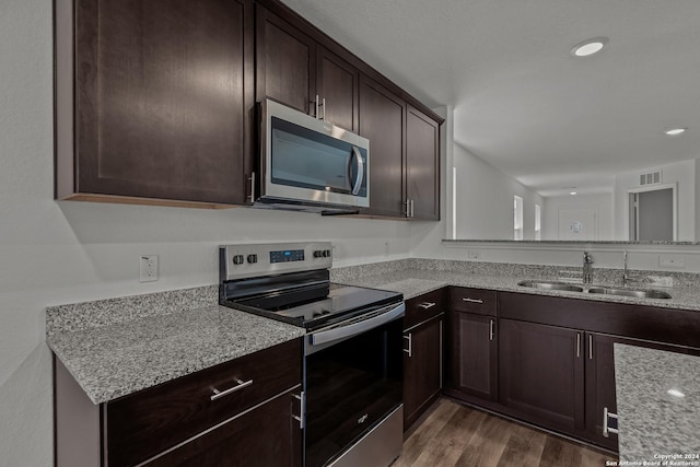 kitchen with sink, light stone counters, dark brown cabinets, dark hardwood / wood-style flooring, and stainless steel appliances