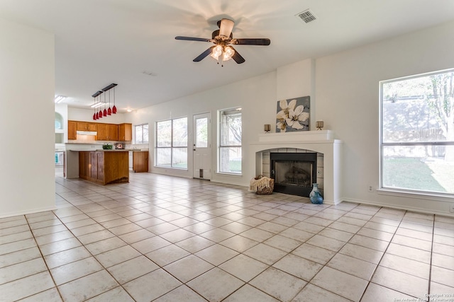 unfurnished living room with ceiling fan, light tile patterned floors, and a tile fireplace