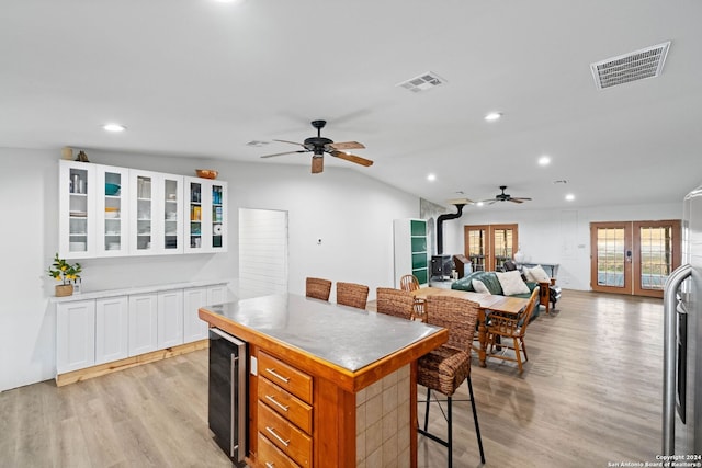 kitchen featuring a wood stove, white cabinetry, french doors, a kitchen breakfast bar, and lofted ceiling