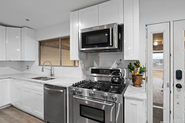 kitchen with white cabinets, appliances with stainless steel finishes, light stone countertops, and sink