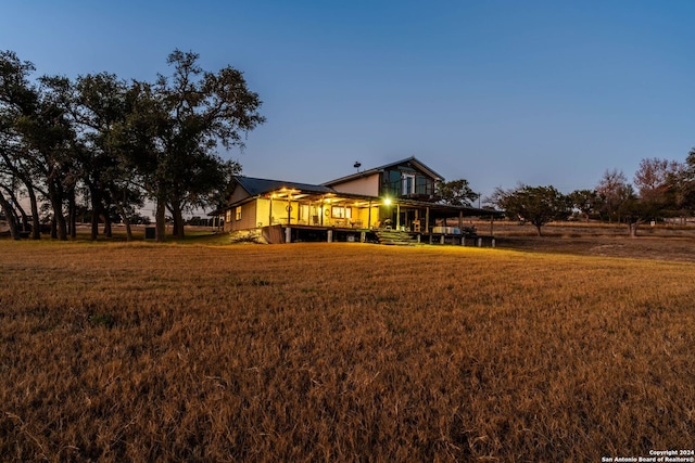 back house at dusk with a lawn and a deck