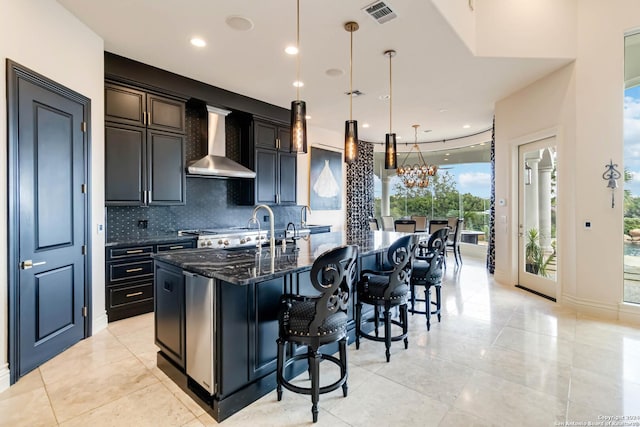 kitchen featuring a kitchen island with sink, a sink, visible vents, wall chimney exhaust hood, and decorative light fixtures