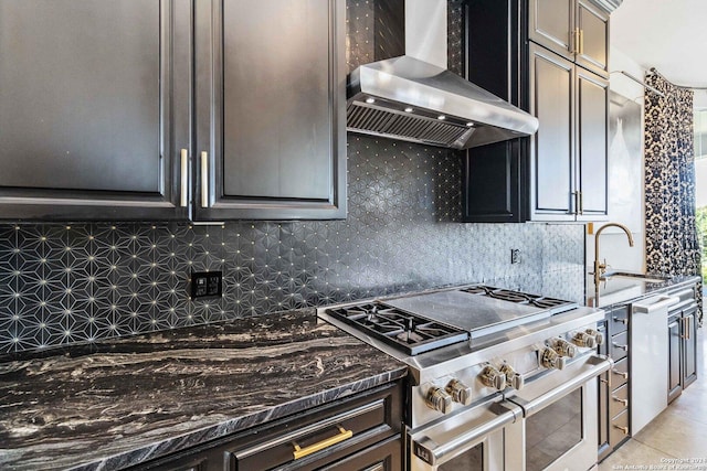 kitchen with backsplash, a sink, wall chimney range hood, dark stone countertops, and double oven range