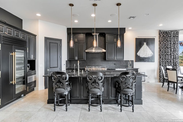 kitchen with decorative light fixtures, visible vents, stainless steel built in fridge, wall chimney range hood, and dark stone counters