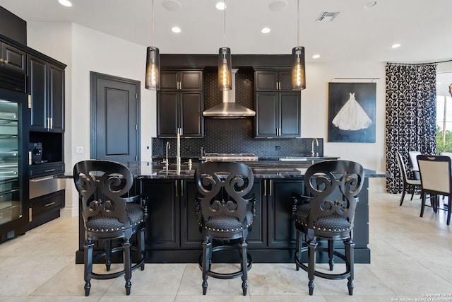 kitchen with visible vents, hanging light fixtures, wall chimney range hood, backsplash, and dark stone countertops