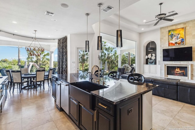 kitchen with decorative light fixtures, visible vents, open floor plan, a kitchen island with sink, and dark stone countertops