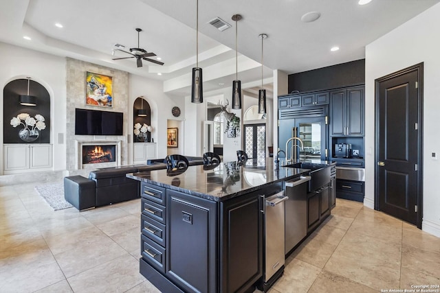 kitchen with a raised ceiling, an island with sink, open floor plan, a fireplace, and a sink