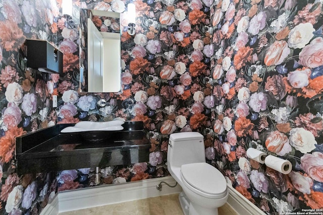 bathroom with a sink, toilet, and wallpapered walls