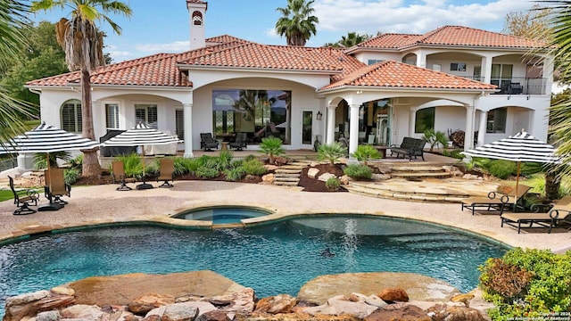 back of house featuring a patio, stucco siding, a balcony, an in ground hot tub, and an outdoor pool