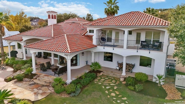 rear view of house with a balcony, stucco siding, a tiled roof, and a patio