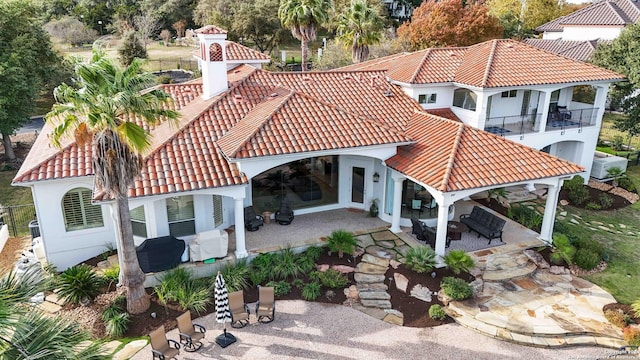 rear view of property featuring a balcony, stucco siding, a tile roof, and a patio