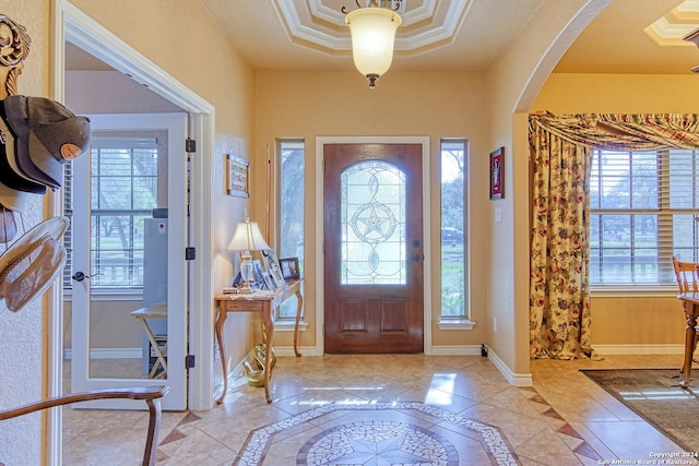 entryway featuring a tray ceiling, a wealth of natural light, and crown molding