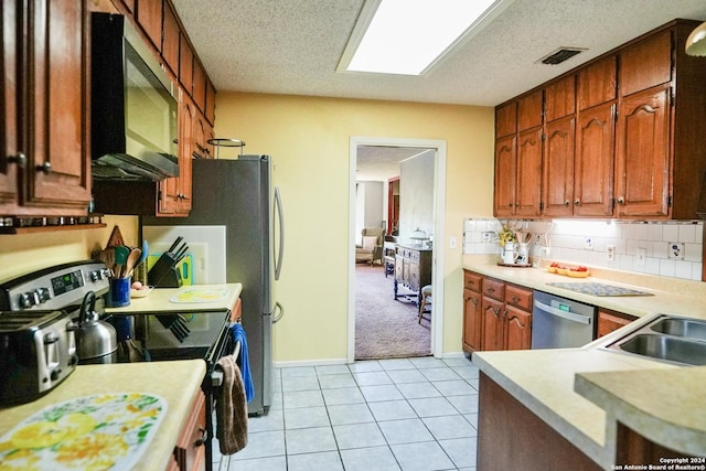 kitchen featuring tasteful backsplash, light tile patterned floors, stainless steel appliances, and a textured ceiling