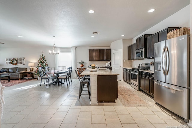 kitchen featuring appliances with stainless steel finishes, a kitchen breakfast bar, a center island with sink, an inviting chandelier, and decorative light fixtures