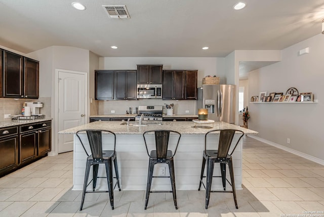 kitchen with dark brown cabinets, stainless steel appliances, a kitchen island with sink, and a kitchen breakfast bar