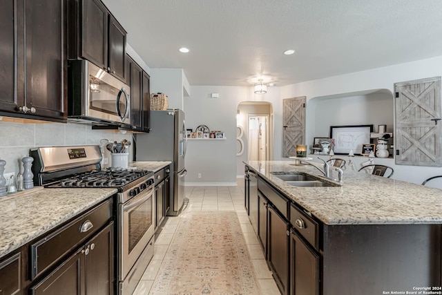 kitchen featuring light stone countertops, sink, an island with sink, light tile patterned floors, and appliances with stainless steel finishes