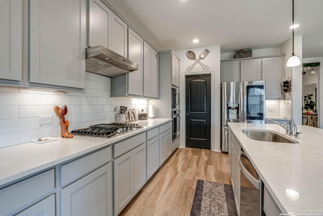 kitchen featuring appliances with stainless steel finishes, light wood-type flooring, tasteful backsplash, sink, and pendant lighting