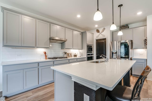 kitchen with light wood-type flooring, stainless steel appliances, sink, pendant lighting, and a center island with sink