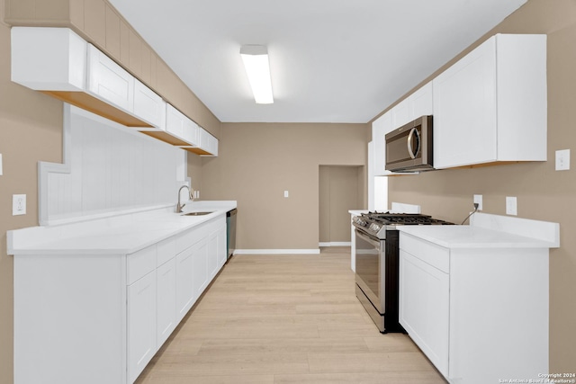 kitchen with white cabinets, appliances with stainless steel finishes, light hardwood / wood-style floors, and sink