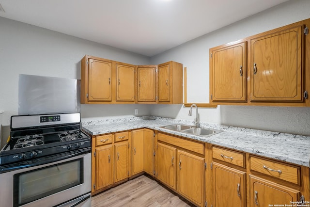 kitchen featuring light wood-type flooring, stainless steel gas stove, light stone counters, and sink