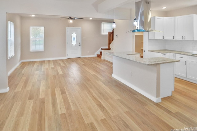 kitchen with island exhaust hood, light stone countertops, pendant lighting, light hardwood / wood-style floors, and white cabinetry