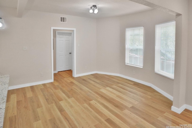 empty room featuring beamed ceiling and light wood-type flooring