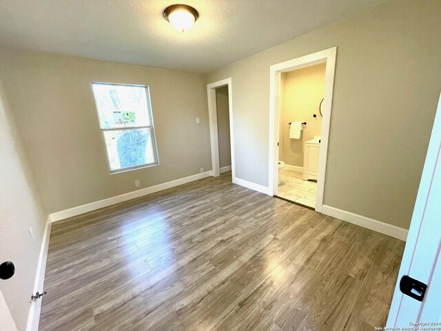 unfurnished bedroom with hardwood / wood-style floors, a textured ceiling, and ensuite bath