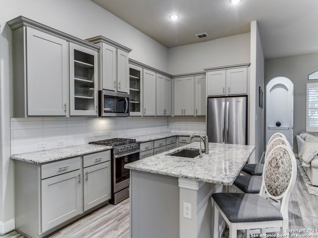 kitchen featuring a kitchen island with sink, sink, tasteful backsplash, light stone counters, and stainless steel appliances